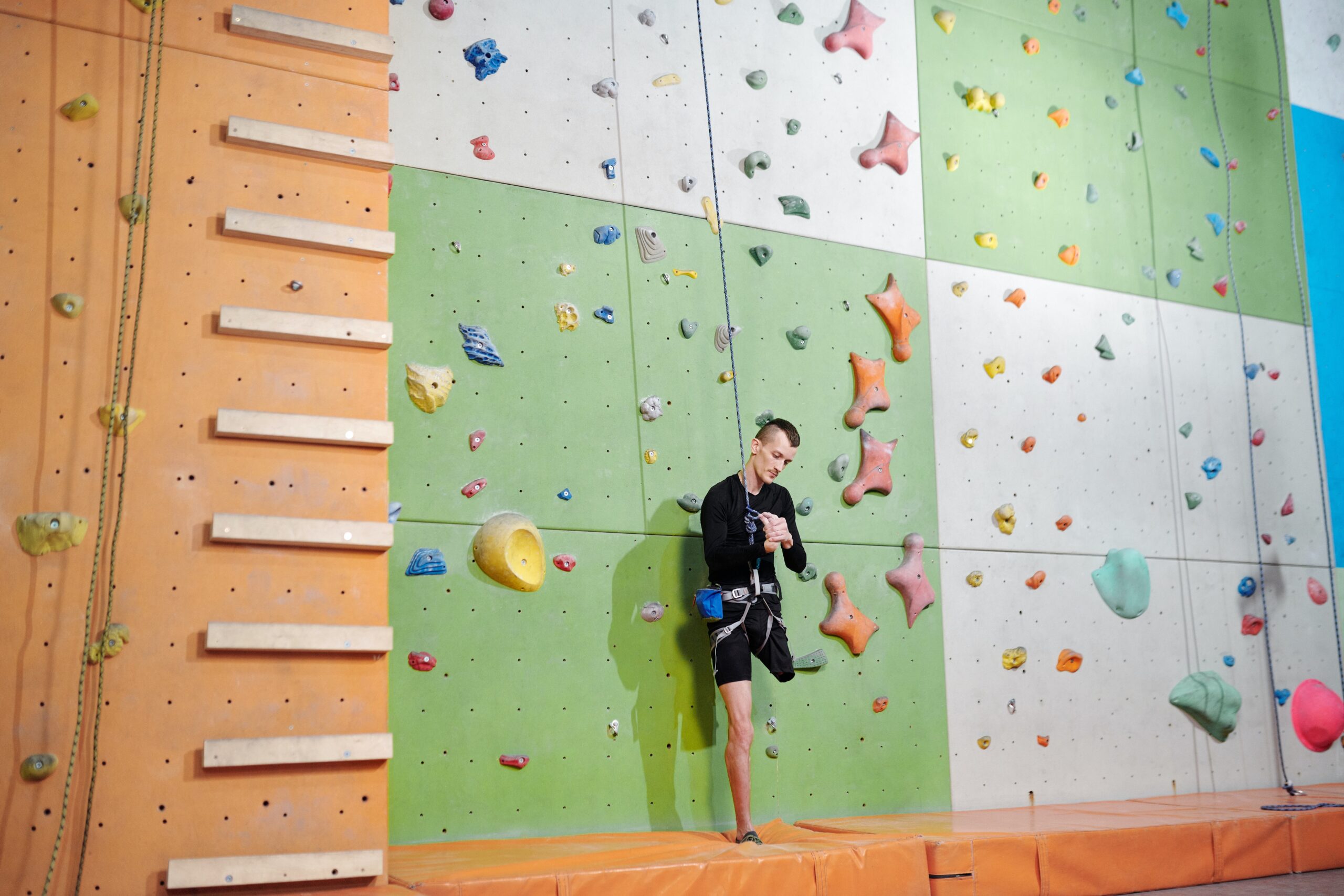 A climber with a lower limb amputation stands at the bottom of a colourful climbing wall.
